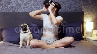 美丽的年轻女子穿着<strong>VR</strong>耳机坐在床上与小狗。 四处看看。 观看<strong>VR</strong>视频，玩<strong>VR</strong>游戏..